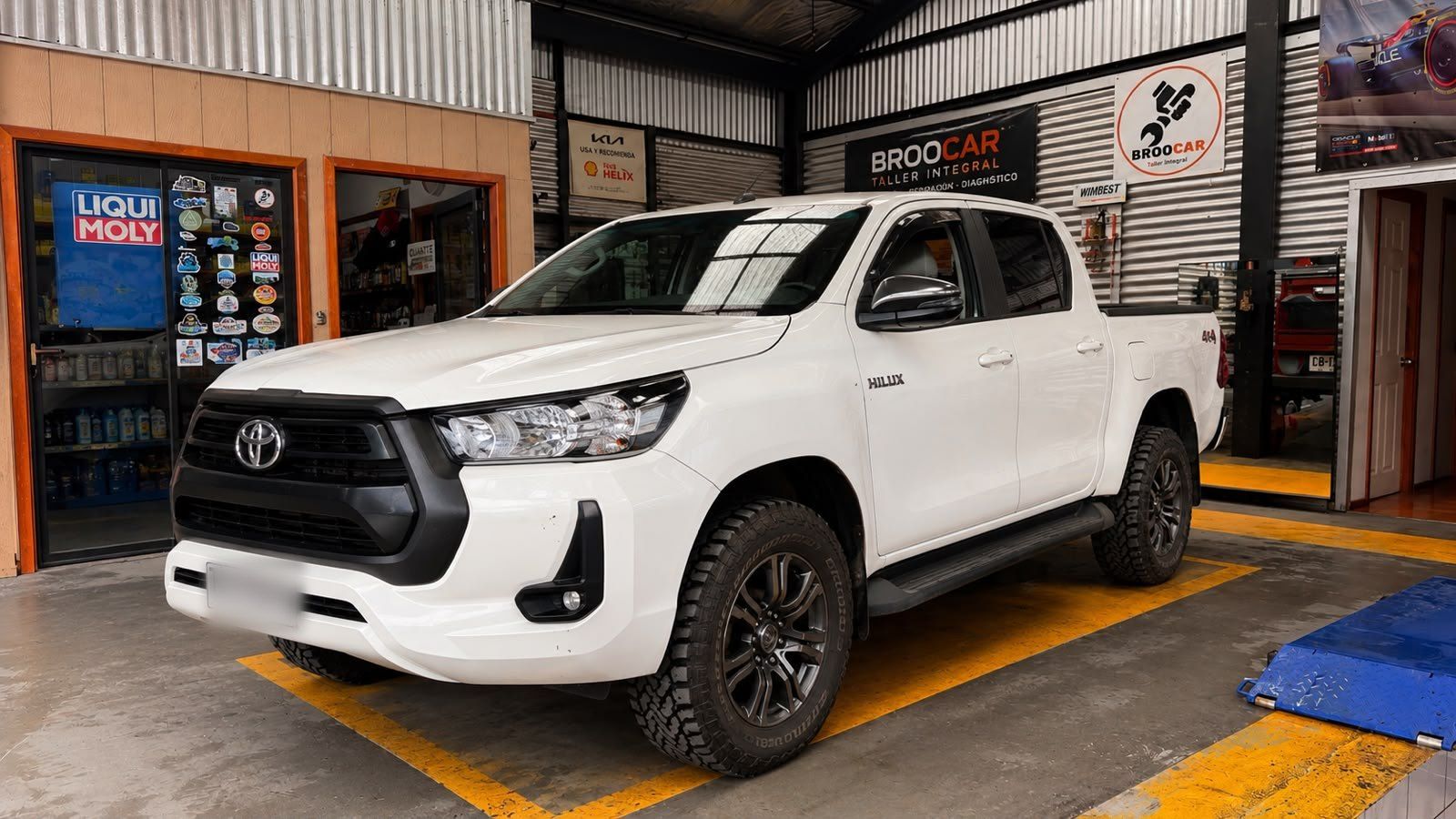 Camioneta Toyota Hilux blanca dentro del taller Broocar, junto al mueble de lubricantes Liqui Moly y la señalética del local